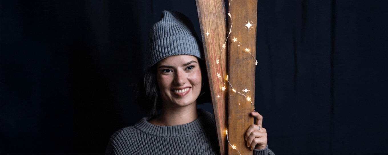 Eine Frau mit grauer Mütze und Pullover hält zwei alte Ski