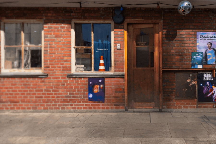 Mann mit Helm und orangefarbener Jacke sitzt auf einem blauen Moped und lächelt in die Kamera 