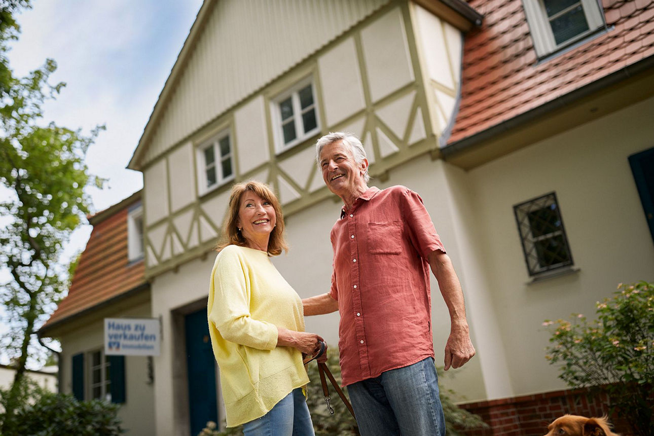 Älteres Ehepaar steht glücklich vor einem Fachwerkhaus