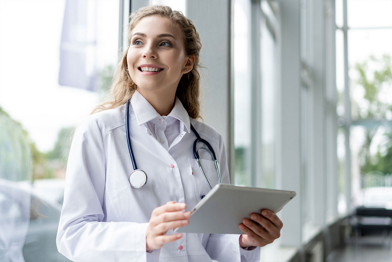 Eine Ärztin mit einem Tablet-PC in der Hand schaut aus Fenster 