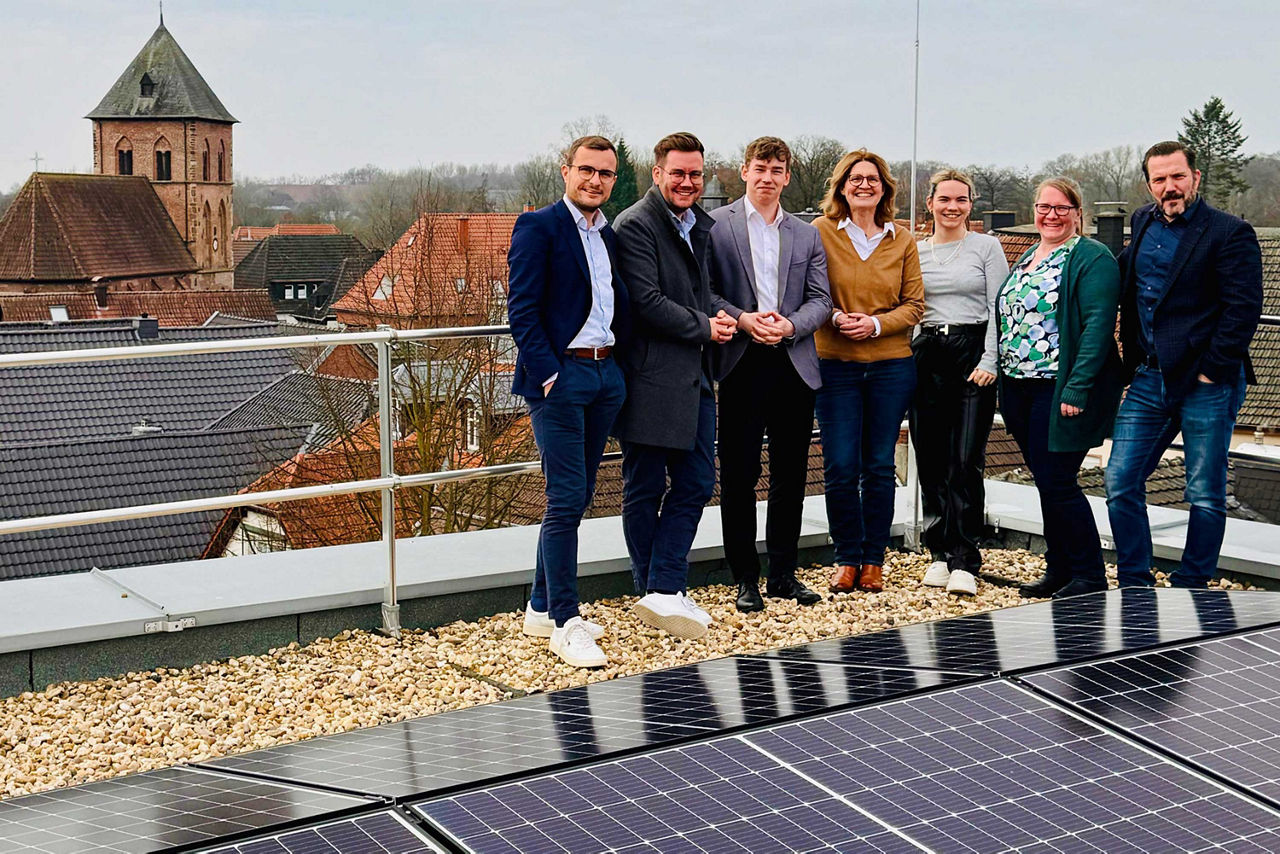 Eine Gruppe von sieben Personen stehend auf einem Dach an einer Solaranlage.