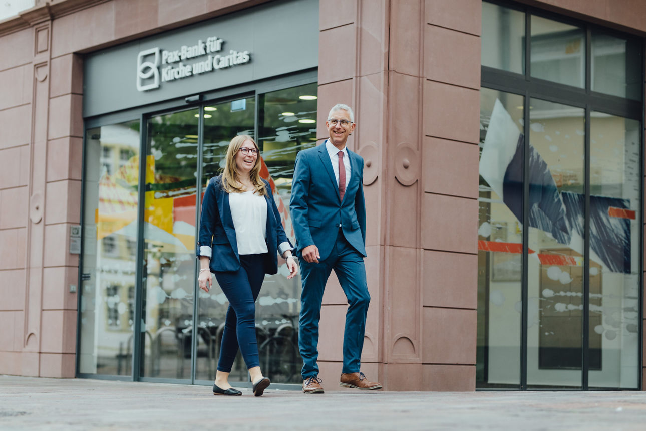 Zwei Mitarbeitende laufen vor der Paderborner Filiale der Pax-BKC entlang