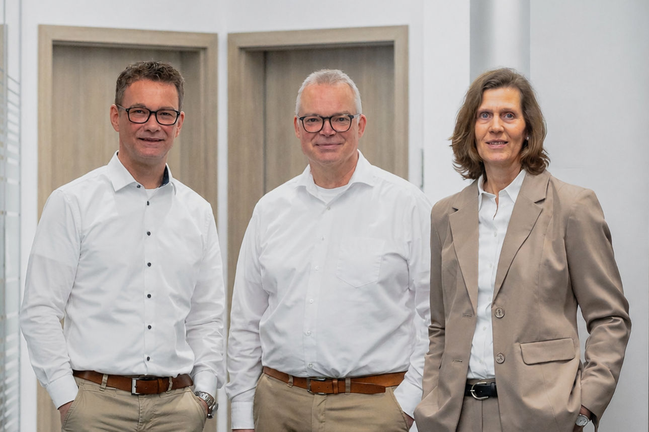 Eine Gruppe von drei Geschäftsleuten, die gemeinsam in einem modernen Büroflur posieren.