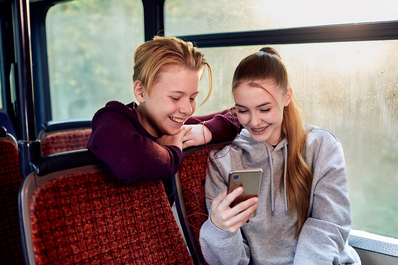 Schüler und Schülerin im Bus wie Sie gemeinsam ins Smartphone schauen.