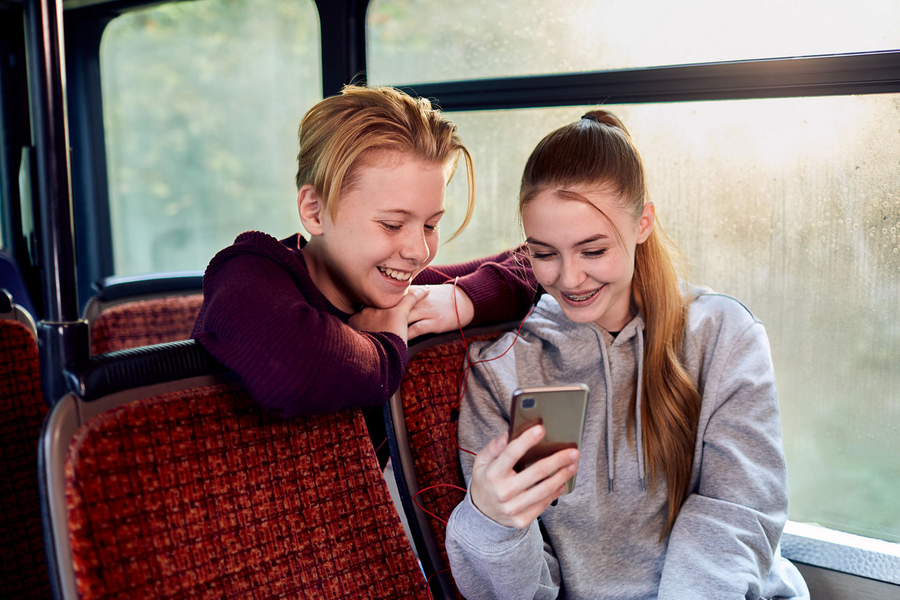 Zwei Kinder sitzen nebeneinander in einem Zug und schauen gemeinsam auf ein Smartphone.