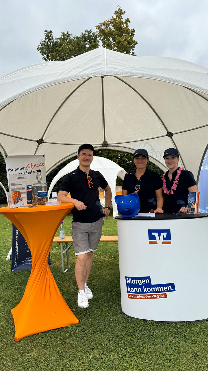 Ein freundliches Team steht unter einem weißen Zelt bei einer Veranstaltung im Freien.