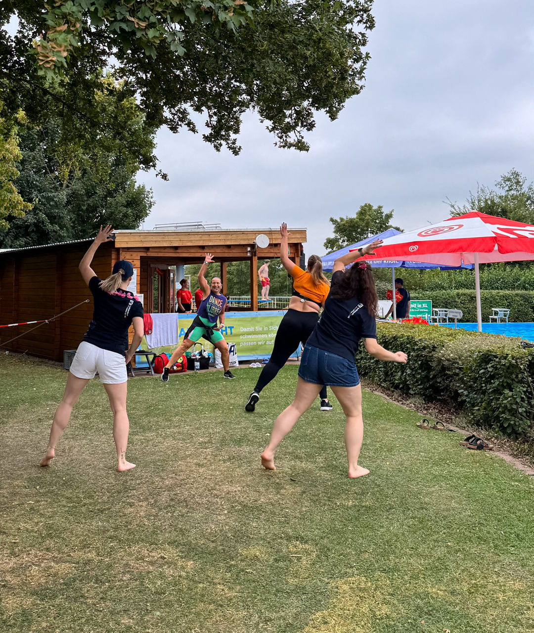 Barfüßige Tänzer springen vor Freude auf einer Rasenfläche neben einem Pool.