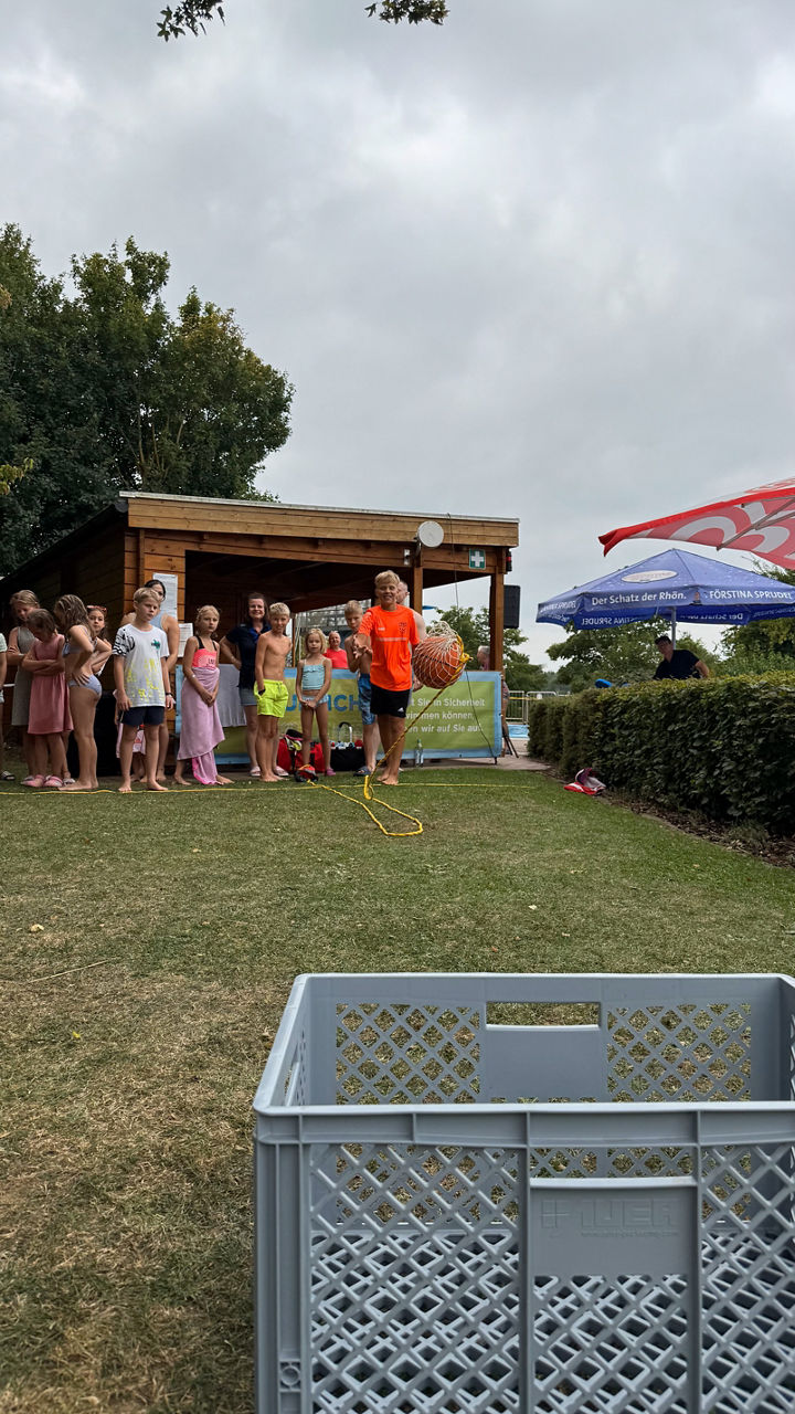 Outdoor-Aktivität mit Kindern in einer Reihe, ein Junge hält einen Netzball an einem Seil.