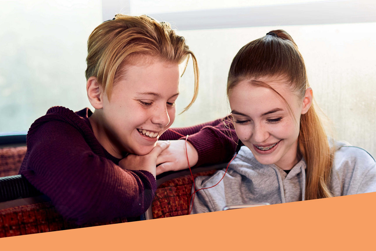 Zwei Jugendliche sitzen im Bus und schauen lächelnd auf ein Smartphone