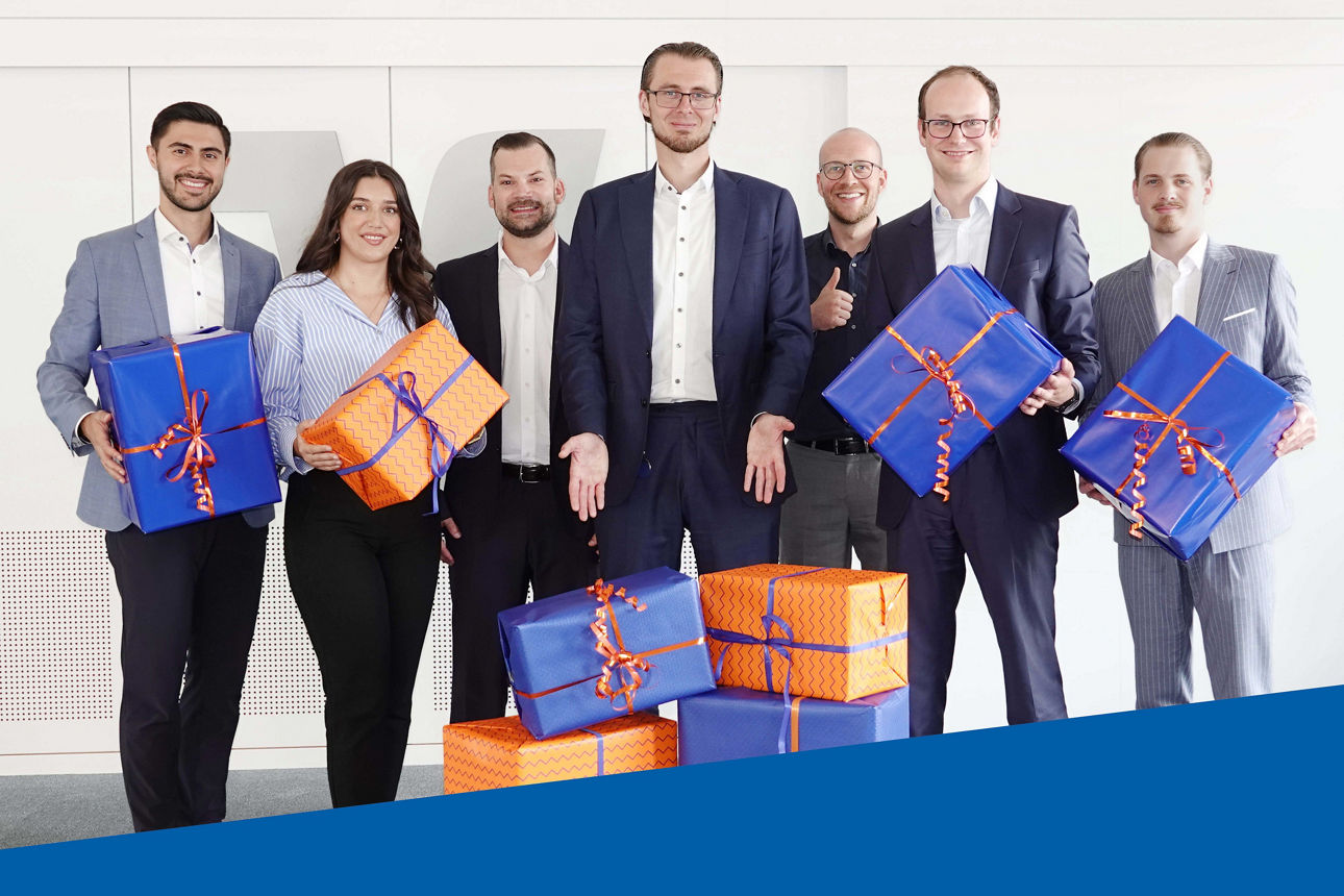 Bild von einer Gruppe von Menschen, die große blaue und orangene Geschenke in der Hand halten. 