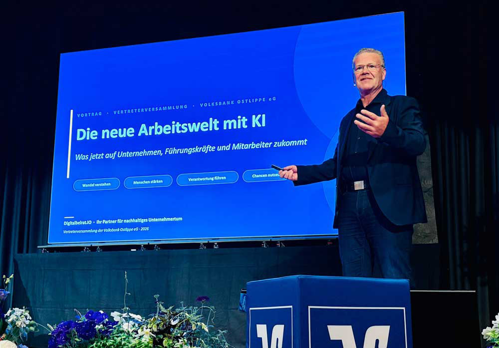Ein Redner hält auf einer Bühne einen Vortrag zum Thema „Die neue Arbeitswelt mit KI“ vor einer großen, blauen Präsentationsl