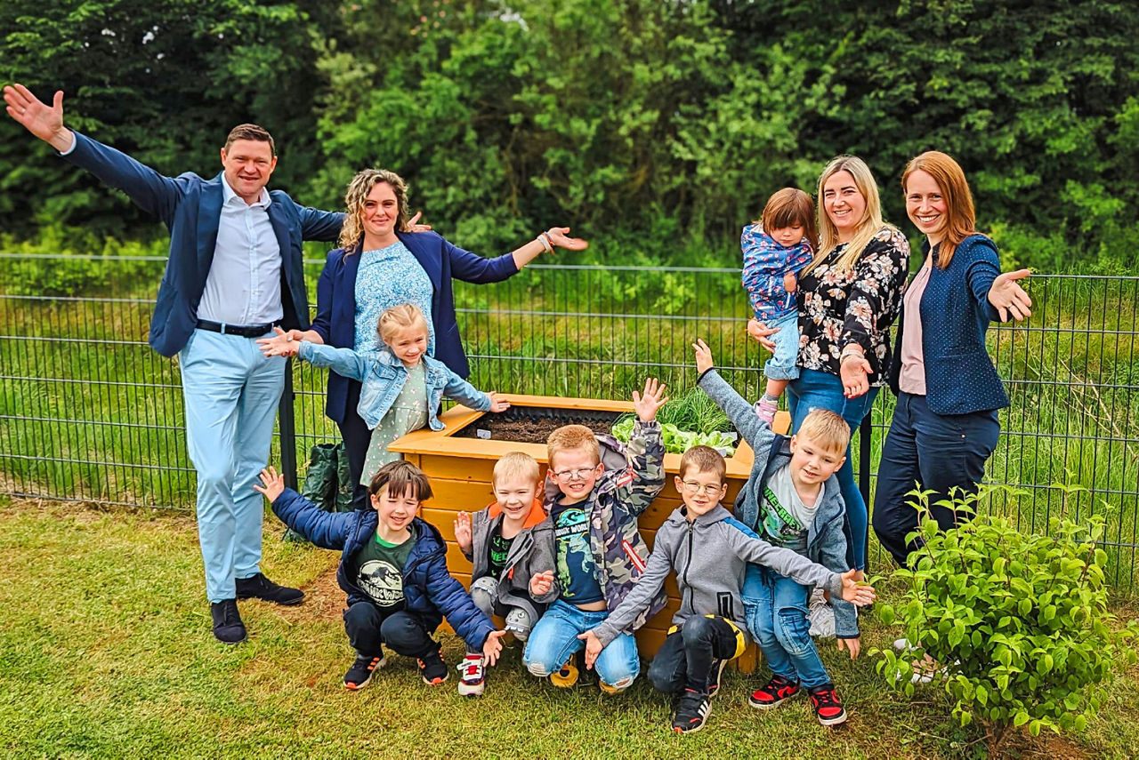 Eine Familie lächelt für ein Foto vor einem lebhaften Garten, der mit Blumen und Grünpflanzen gefüllt ist.