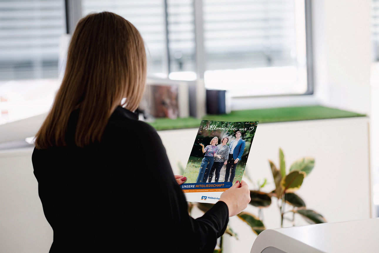 Frau steht mit dem Rücken zur Kamera und hält das Magazin "Willkommen bei uns" in der Hand.