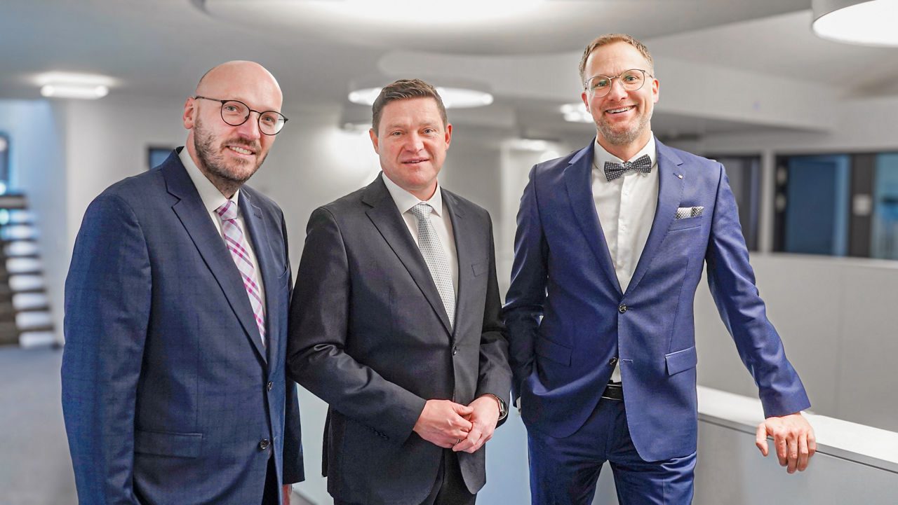 Drei Männer in Geschäftsanzügen posieren für ein Foto in einer Büroumgebung