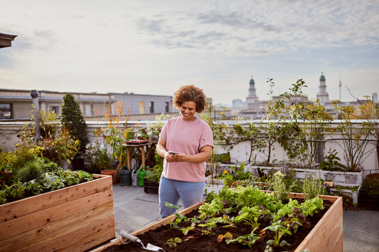 Frau steht auf einer Dachterrasse mit einem Smartphone in der Hand