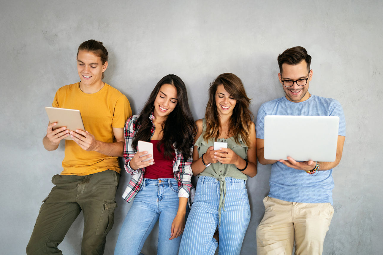 Eine Gruppe von vier Menschen steht an einer Wand mit einem Laptop, Tablet oder Handy in der Hand