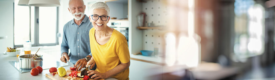 Ein Mann und eine Frau lächeln beim Kochen in die Kamera