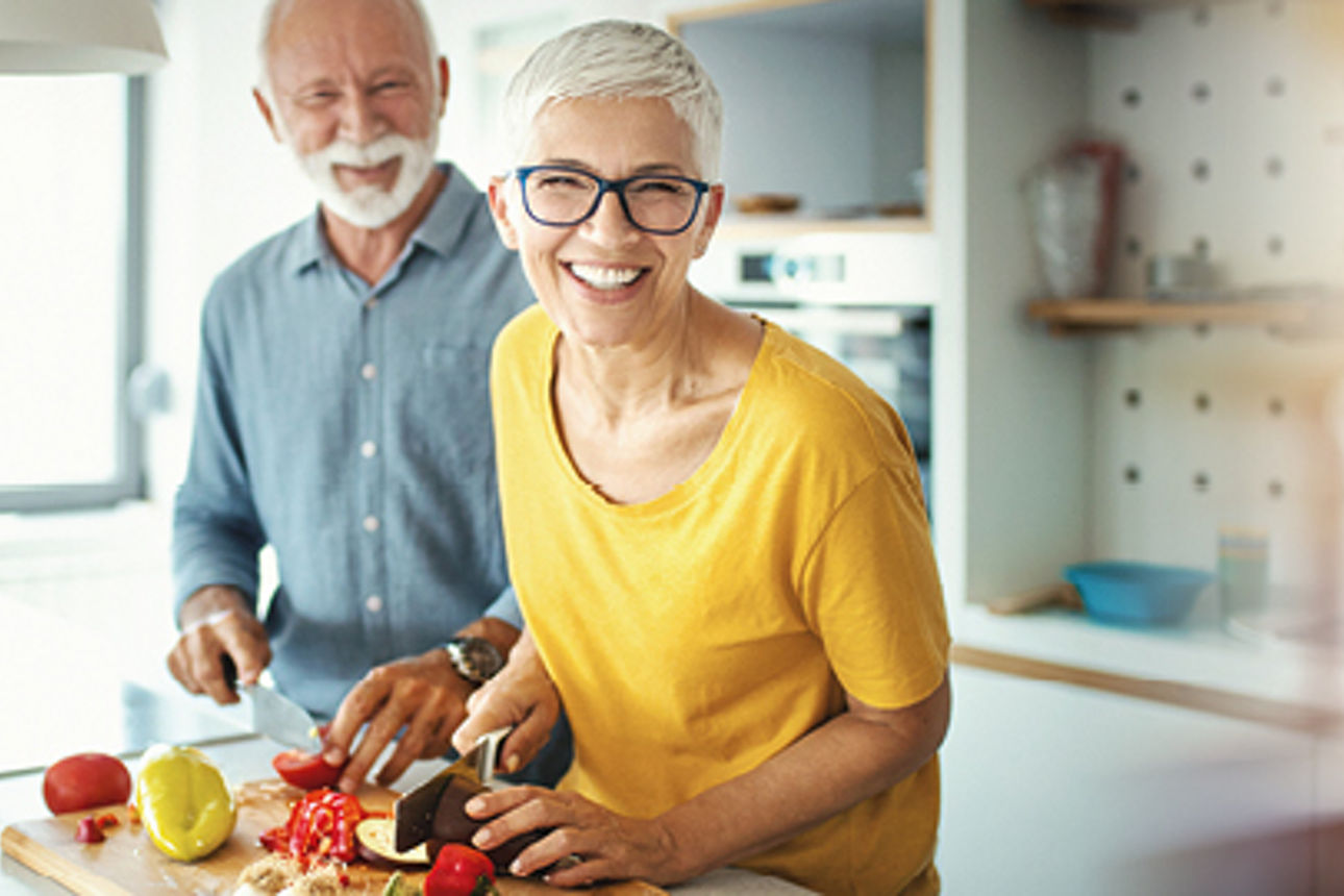 Ein Mann und eine Frau lächeln beim Kochen in die Kamera