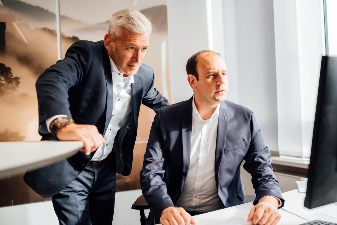 Zwei Männer in Anzügen arbeiten gemeinsam an einem Computer in einem modernen Büro