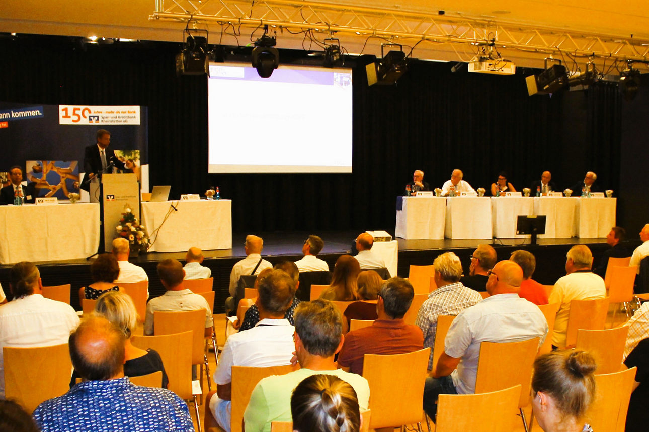 Sitzreihen mit Personen die auf die Bühne schauen.