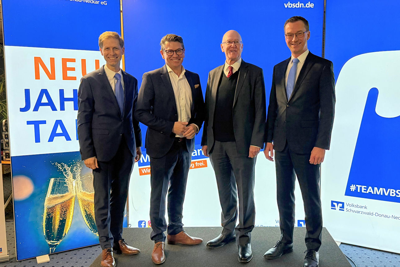 Vier männliche Führungskräfte in Business-Kleidung posieren auf einer kleinen Bühne.