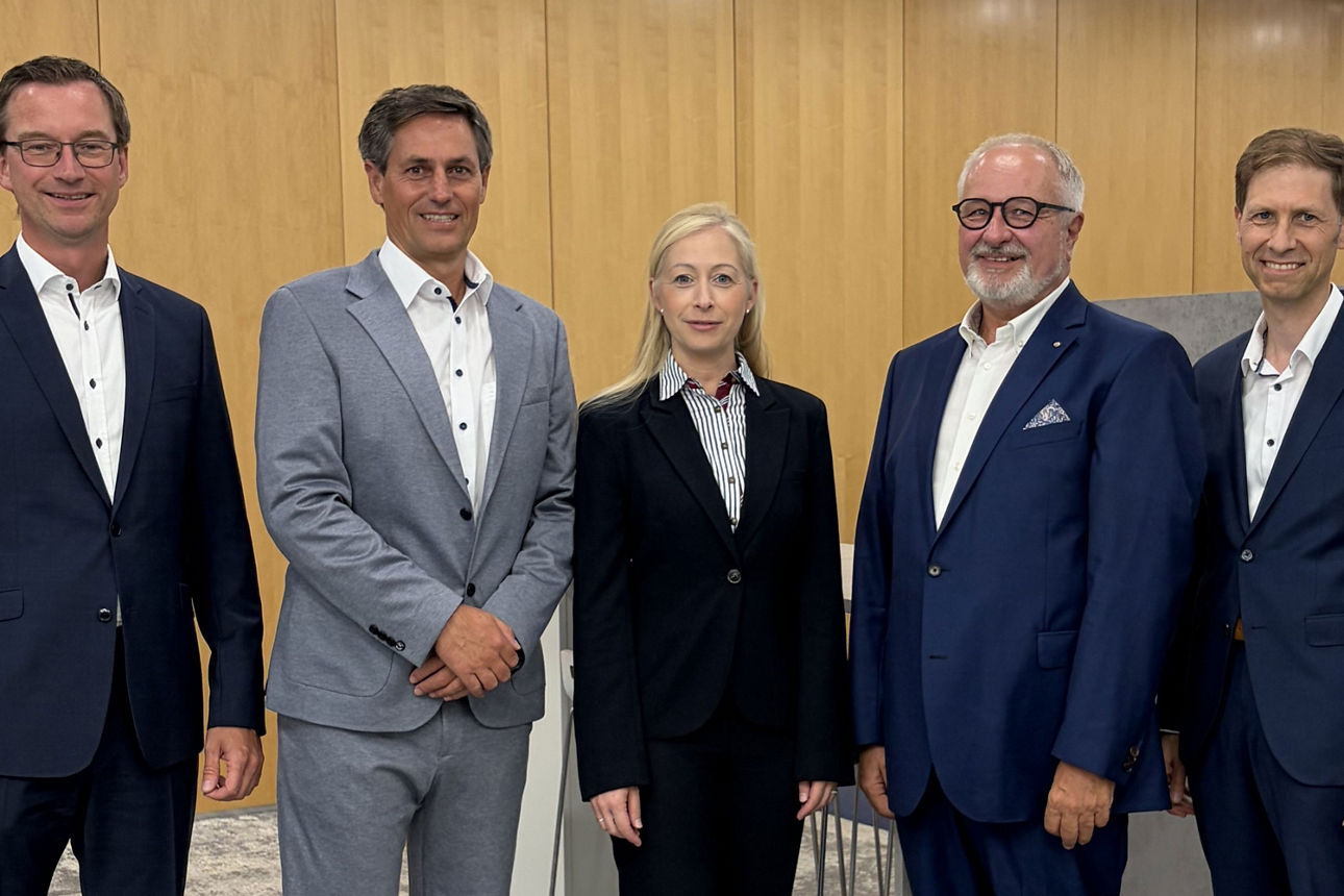 Fünf Personen in Business-Kleidung posieren vor einer Wand