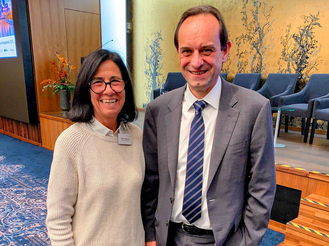 Vorständin Anette Waidelich im Gespräch mit Mark Branson, Präsident der Bafin nebeneinander vor einer Bühne.