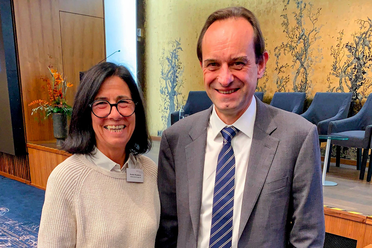 Vorständin Anette Waidelich im Gespräch mit Mark Branson, Präsident der Bafin nebeneinander vor einer Bühne.