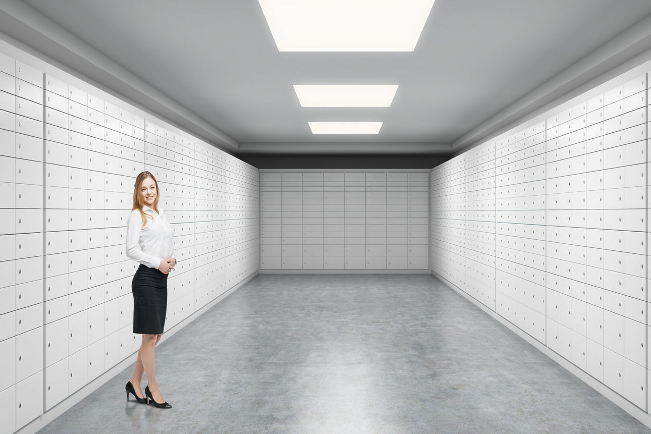 A beautiful private manger of a bank is standing in a room with safe deposit boxes. A concept of storing of important documents or valuables in a safe and secure environment.