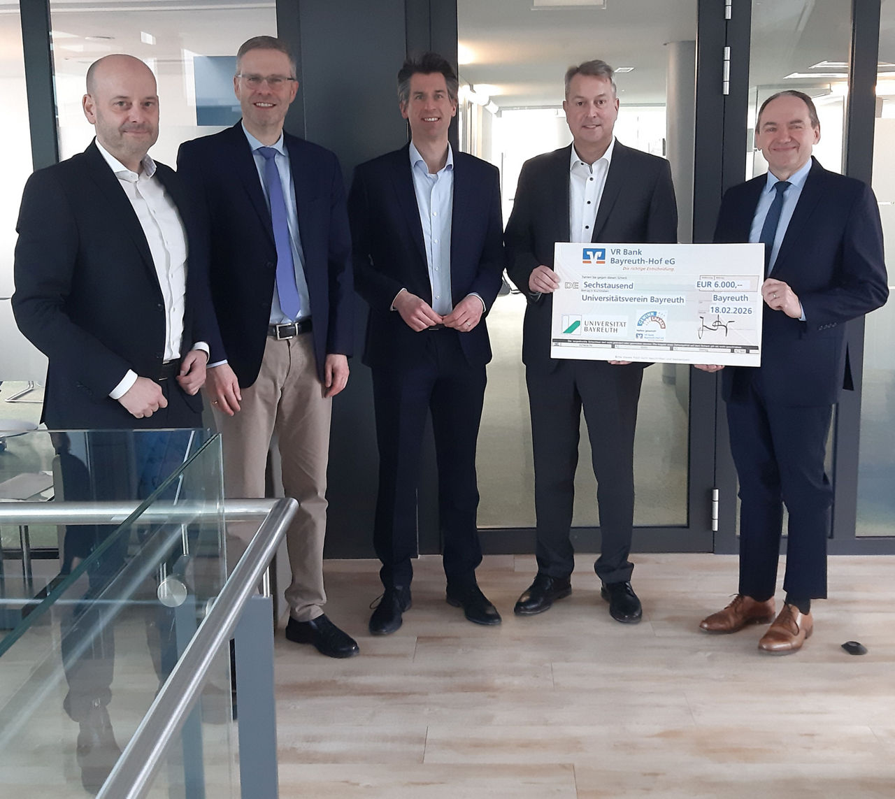 Fünf Personen stehen zusammen und halten einen großen symbolischen Spendenscheck in den Händen.