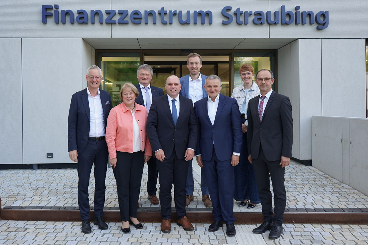 6 Männer in Anzügen und 2 Frauen stehen vor Gebäude mit Aufschrift Finanzzentrum Straubing