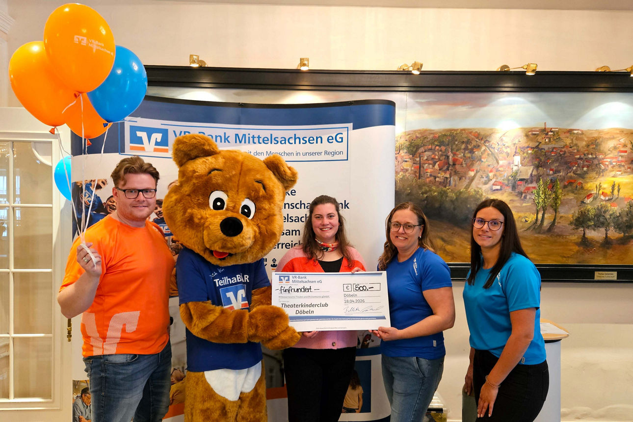 Zwei Frauen, ein Mann und ein Maskottchen überreichen einer Vertreterin des Theaters Döbeln ein Spendenscheck 