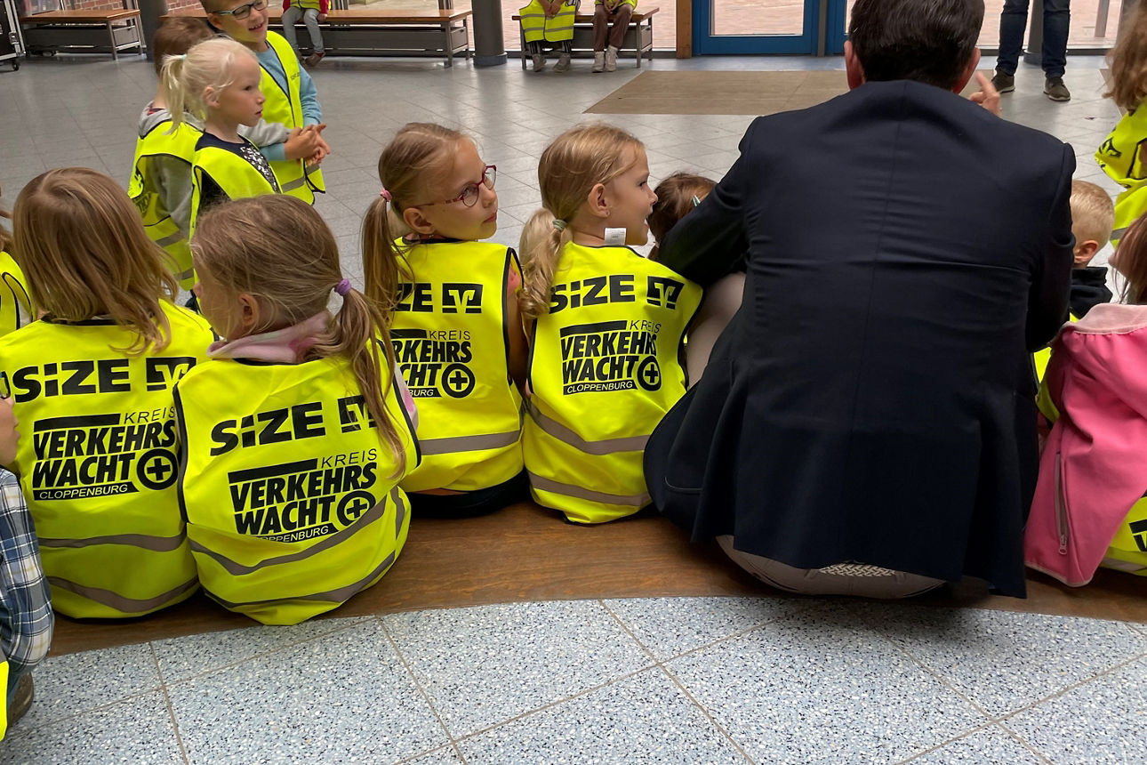 Vorstand sitzt zwischen Kindern bei der Warnwesten-Übergabe
