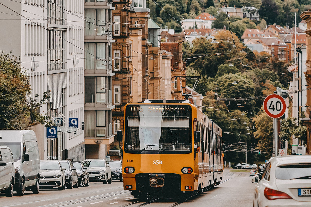 Gelber Stadtbahnzug der SSB fährt durch eine Straße mit geparkten Autos und 40er-Schild, im Hintergrund grüne Hügel und Häuser.