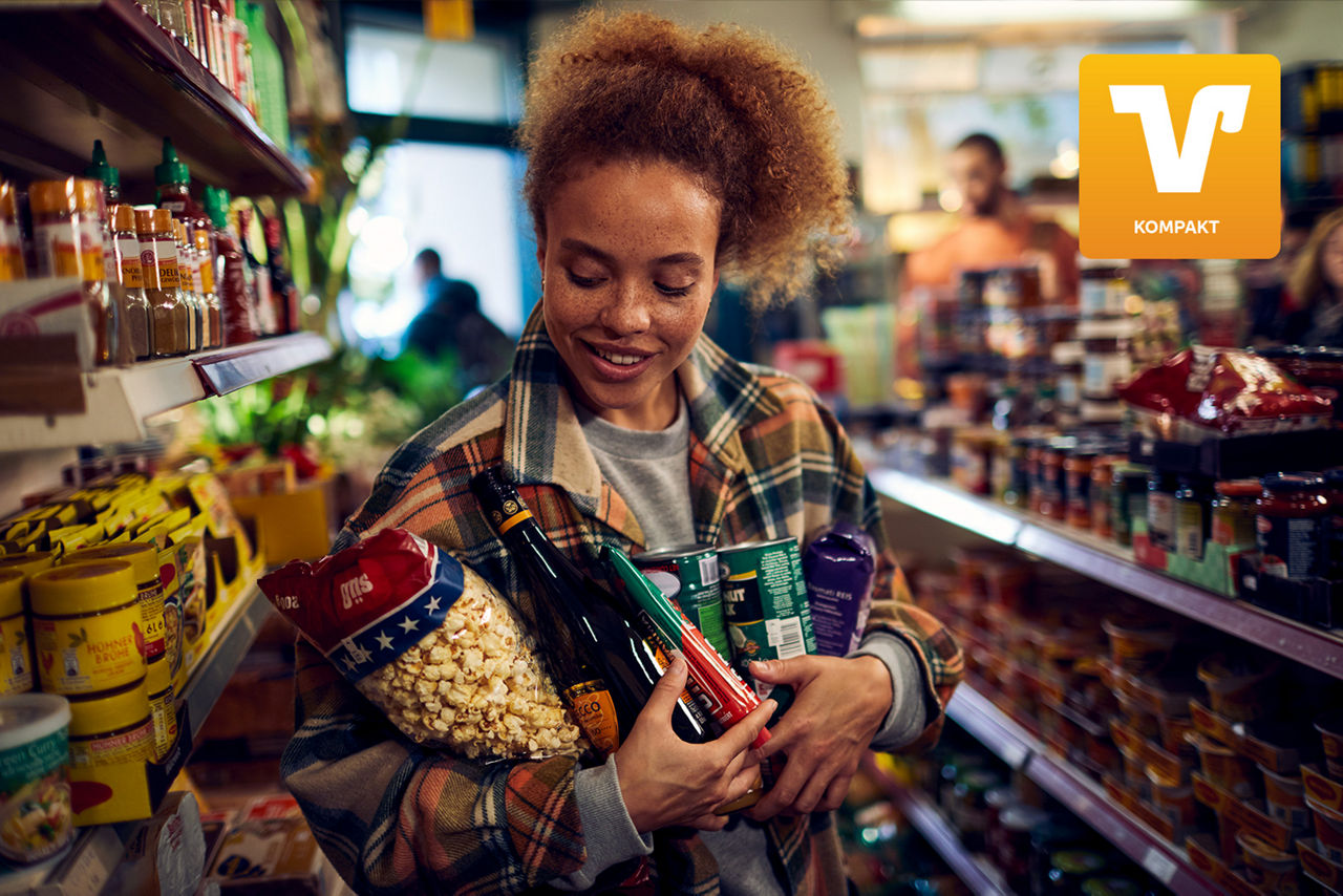Junge Frau zwischen Supermarktregalen mit Einkäufen auf dem Arm