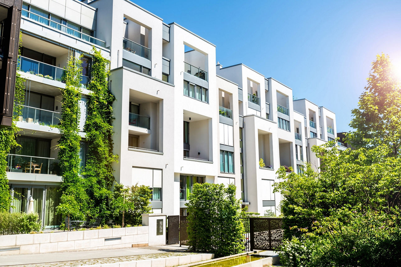Foto von einem modernen Mehrfamilienhaus mit Büschen und Bäumen bei Sonnenschein