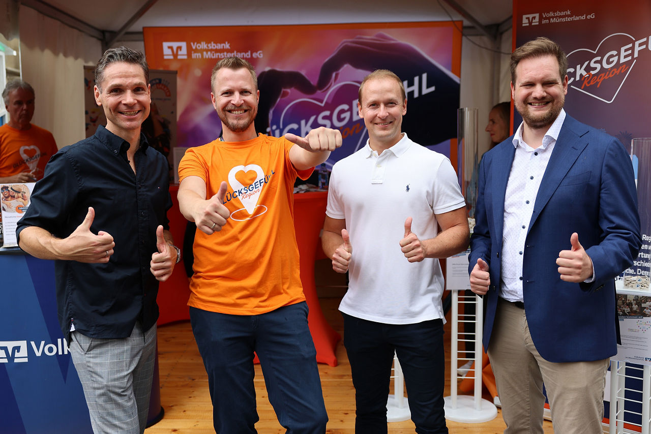 Mitarbeiter der Volksbank im Münsterland und des Gewinnsparvereins stehen auf dem Stadtfest in Münster und halten Daumen hoch
