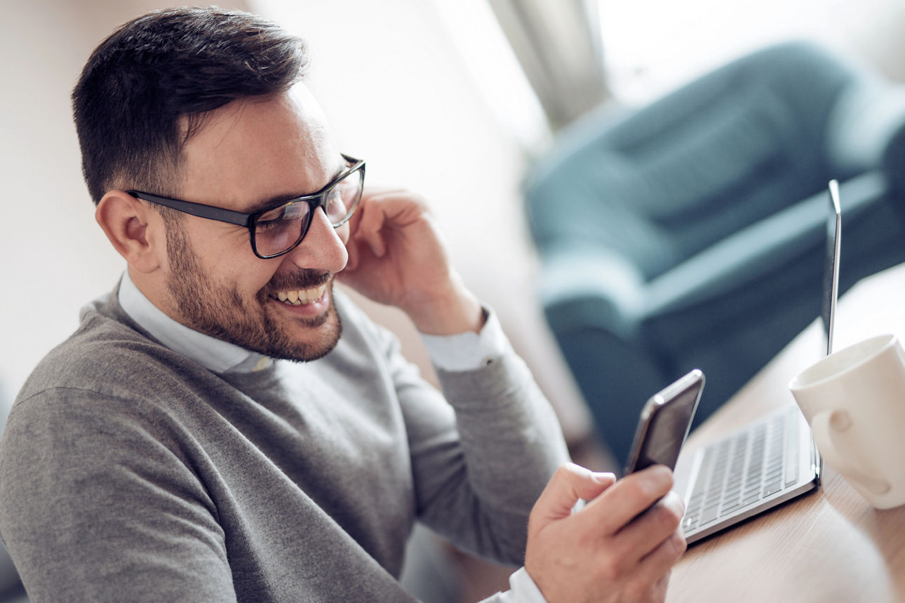 Mann sitzt lächelnd am Tisch und schaut auf sein Handy
