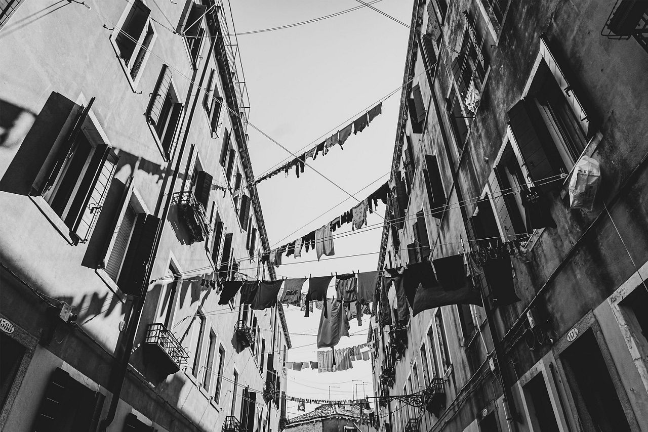 Blick nach oben zwischen zwei hohen Häuserreihen mit vielen Wäscheleinen, an denen Kleidung hängt.