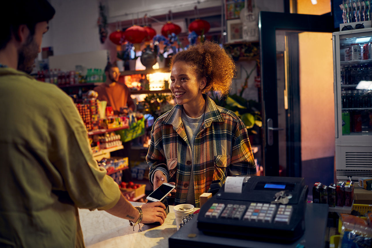 Eine Frau steht im Lebensmittelgeschäft an der Kasse und bezahlt mit dem Handy