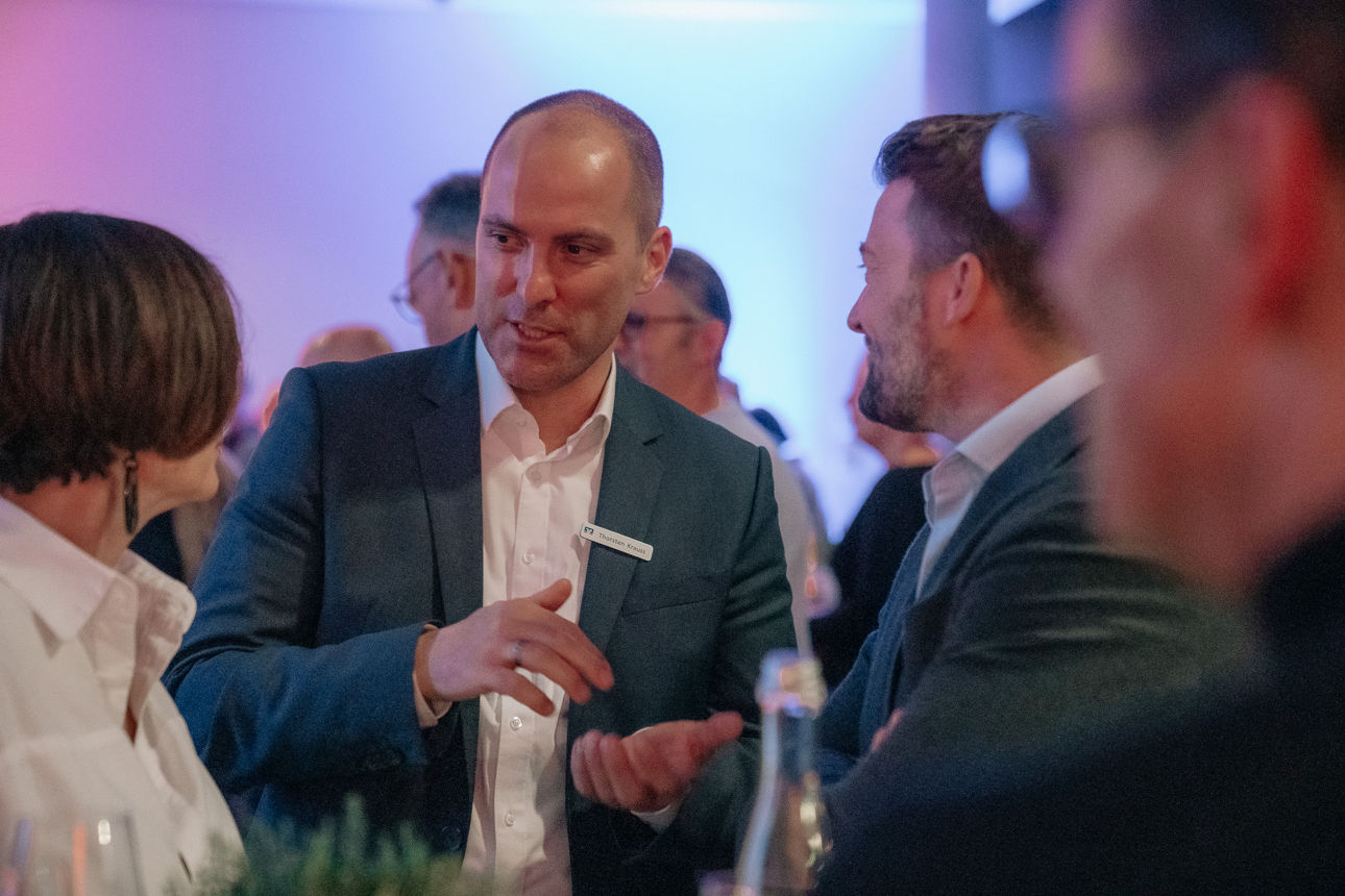 Mann im Gespräch mit Gästen bei einer Abendveranstaltung in lockerer, professioneller Atmosphäre.