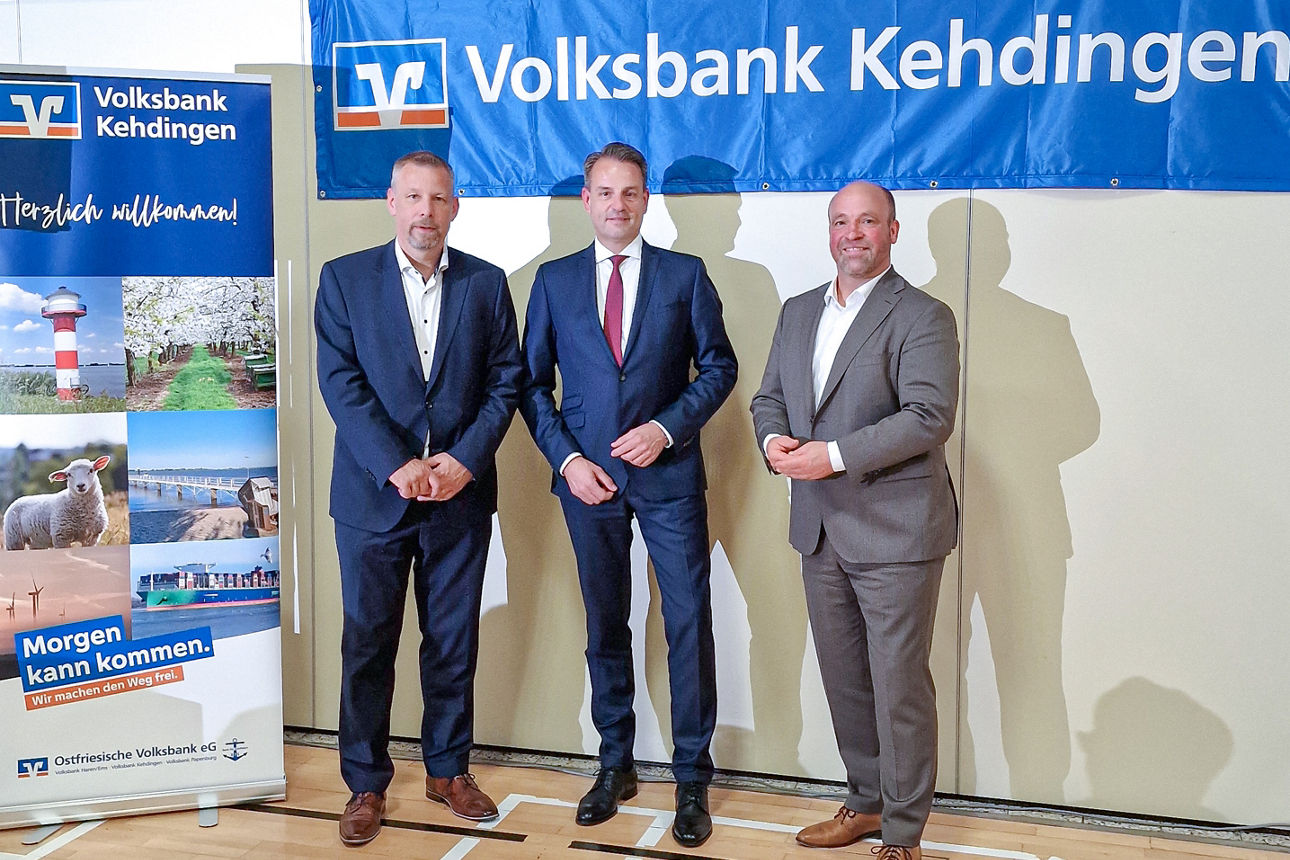 Drei Personen vor Banner der Volksbank Kehdingen, links Display mit ‚Morgen kann kommen‘-Motiv.