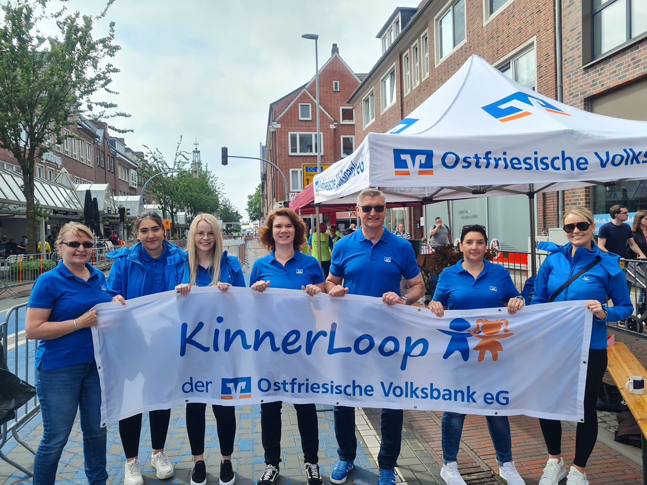 Sieben Personen mit Banner „KinnerLoop der Ostfriesische Volksbank eG“ vor Zelt mit Banklogo