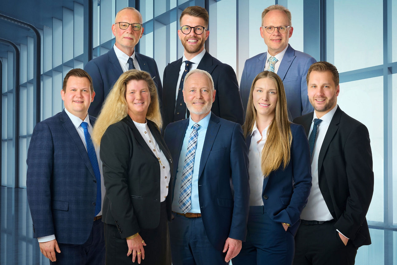 Acht Personen in Business-Kleidung blicken freundlich lächelnd in die Kamera