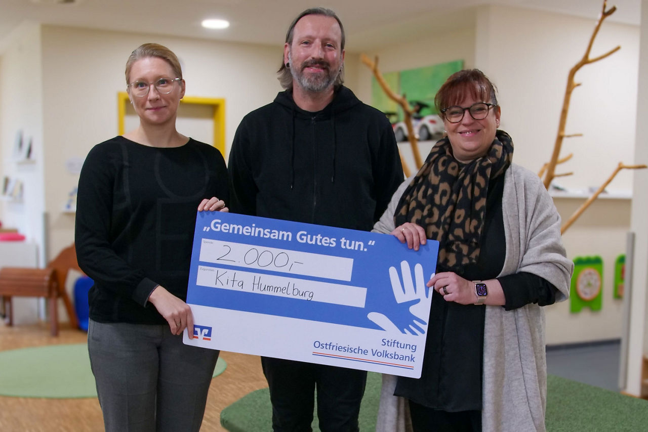 Andrea Wilken, Thomas Janssen und Tessa Duve Nanninga stehen im Flur der Krippe und halten einen symbolischen Scheck