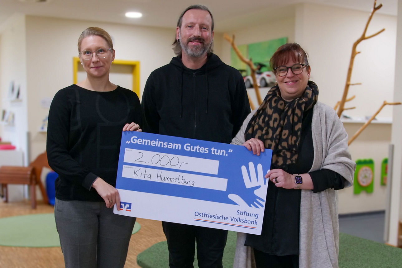 Andrea Wilken, Thomas Janssen und Tessa Duve Nanninga stehen im Flur der Krippe und halten einen symbolischen Scheck