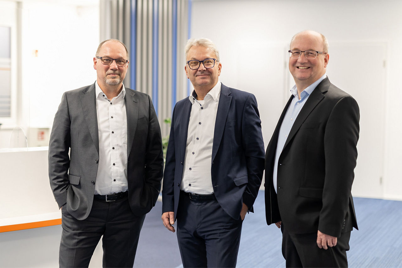 Drei Männer stehen nebeneinander in einem professionellen Büro