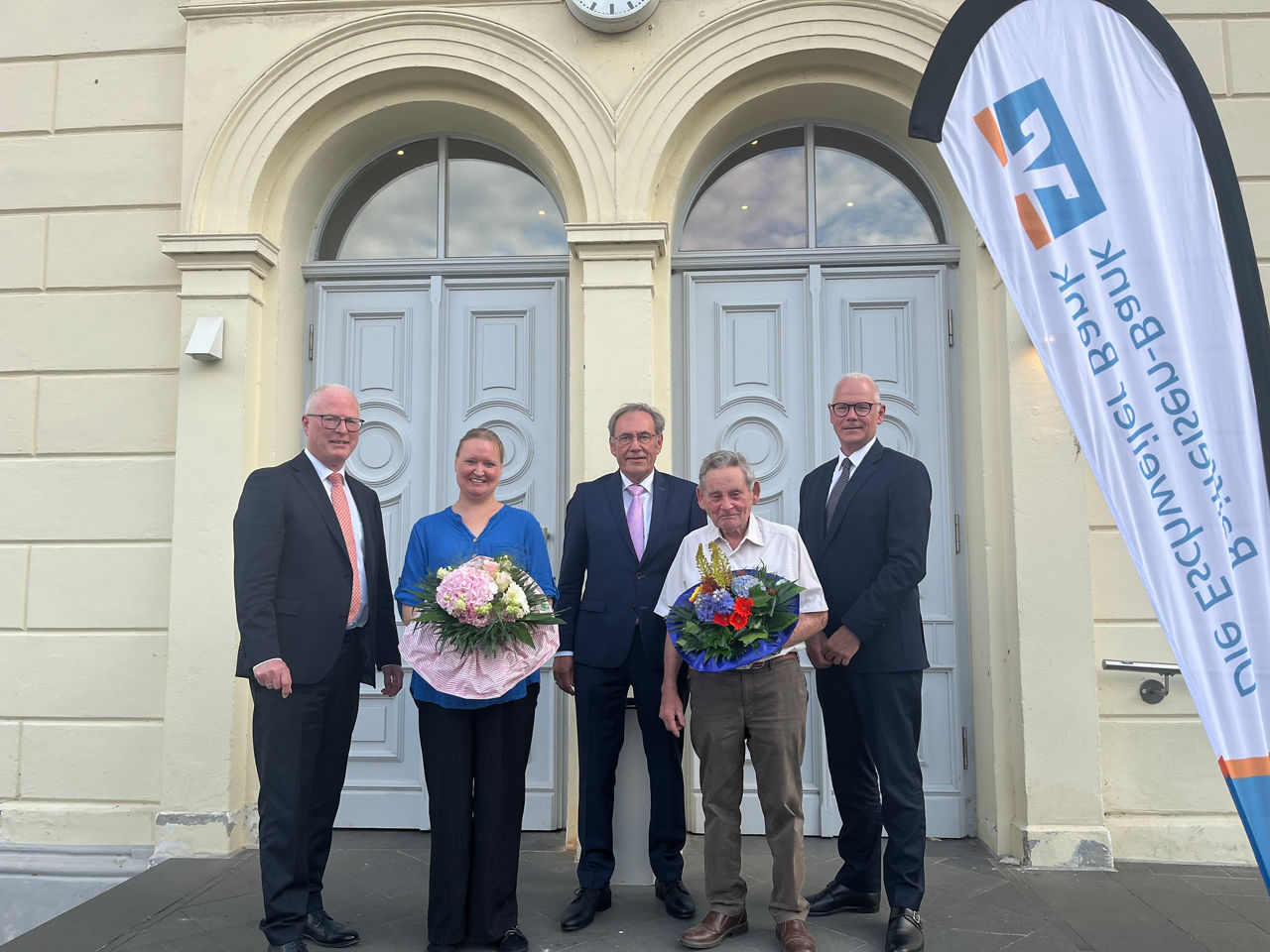 Förmliche Kleidung und ein festlicher Blumenstrauß kennzeichnen ein wichtiges Ereignis in der Bank.