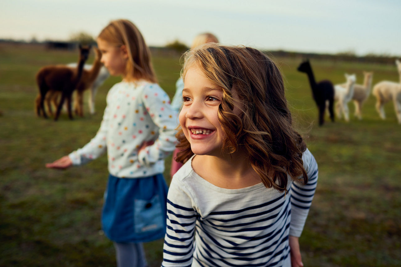 2 Kinder auf einer Wiese im Hintergrund sind Alpakas