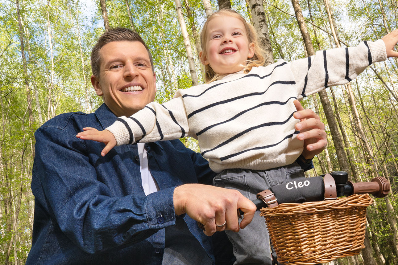 Vater mit seiner Tochter, die auf einem Fahrrad die Arme ausbreitet